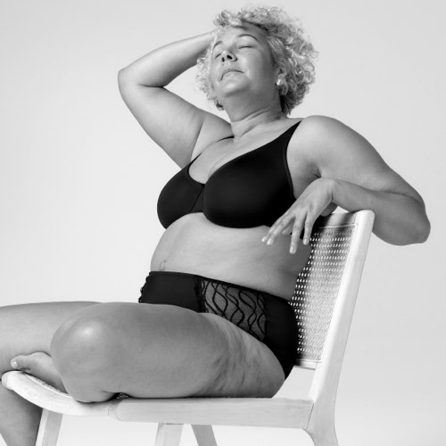 Woman sitting on a chair wearing TENA Silhouette Washable Absorbent Underwear and a bra.